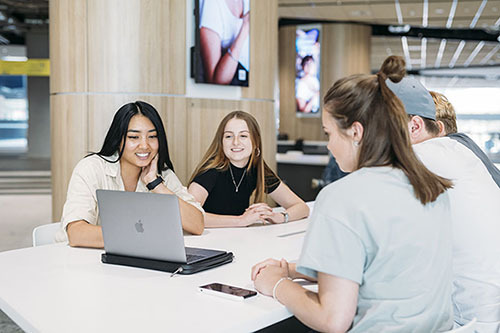 University students sit together around a table looking at a laptop