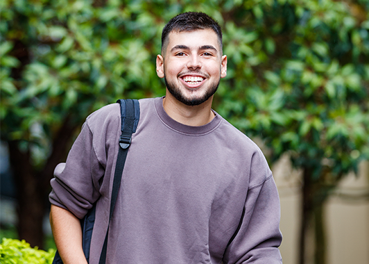 Male student with backpack on his shoulder smiling at the camera