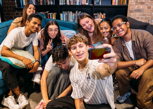Group of students sitting on a couch and taking a selfie in front of a bookshelf