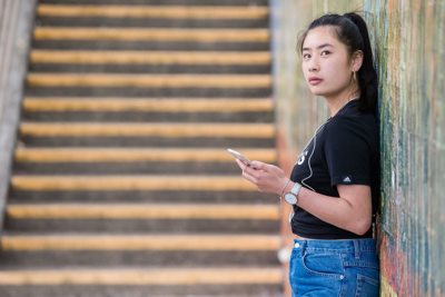 Girl leaning against a wall, holding a mobile phone and staring into the camera