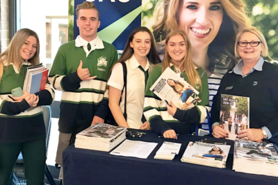 Four uniformed school students stand with UAC staff member at expo. Four uniformed school students stand with UAC staff member at expo.