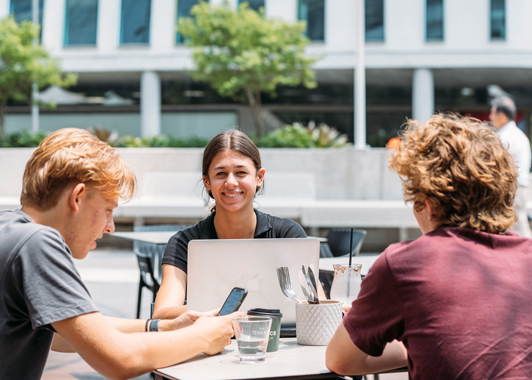 Three students sitting at an outside table with a laptop