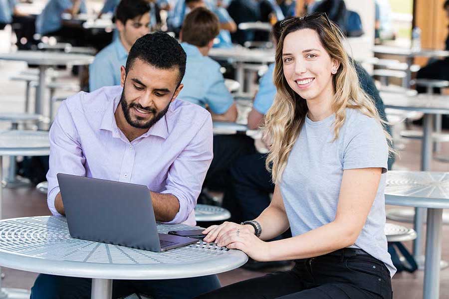 Guy sitting at a café looking at a laptop and a girl sitting beside him looking at the camera Guy sitting at a café looking at a laptop and a girl sitting beside him looking at the camera