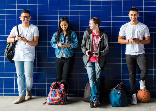 Four smiling young people standing in front of tiled blue wall Four smiling young people standing in front of tiled blue wall