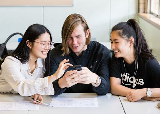 Three young people, a guy and two girls, huddle over a mobile phone smiling