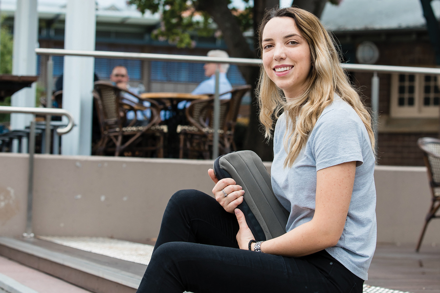 Young woman sitting on stairs outside smiling and facing camera; she holds a laptop in laptop case close to her. Young woman sitting on stairs outside smiling and facing camera; she holds a laptop in laptop case close to her.