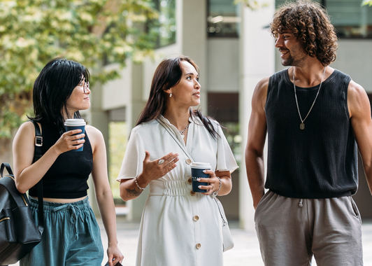 Three students walking and chatting outside holding coffees