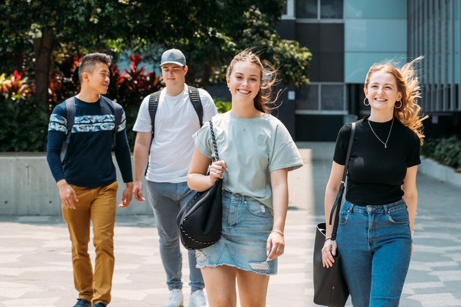 Four young uni students walking towards camera outside