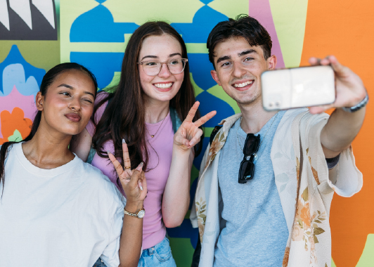 Three students waiting for their uni offer, taking a selfie in front of a colourful mural