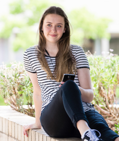 Girl with striped t-shirt leaning back with one knee up on a low brick wall outside Girl with striped t-shirt leaning back with one knee up on a low brick wall outside