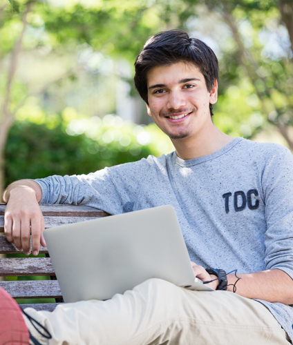 Guy with laptop reclining with one arm resting and legs up on a park bench, smiling to camera Guy with laptop reclining with one arm resting and legs up on a park bench, smiling to camera