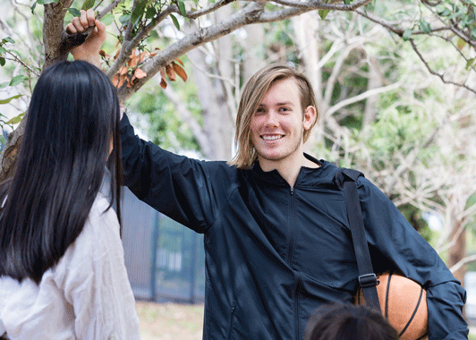 Guy holding basketball smiles under a tree with girl facing away from the camera Guy holding basketball smiles under a tree with girl facing away from the camera